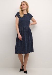 Navy blue lace dress with short sleeves, fitted bodice, flared skirt, scalloped hemline, and floral pattern details throughout.