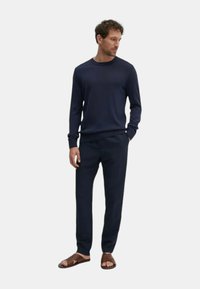 Chemise à manches longues bleu marine en tissu doux, associée à un pantalon assorti et des sandales à glissière marron, offrant une coupe décontractée et un design minimaliste.