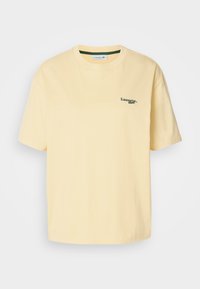 T-shirt en coton jaune avec une coupe décontractée, des manches courtes et un logo brodé vert sur la poitrine gauche. Texture lisse, col rond.