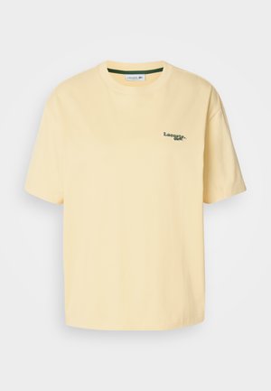 T-shirt in cotone giallo con vestibilità rilassata, maniche corte e logo ricamato verde sul lato sinistro del petto. Texture liscia, colletto a giro.