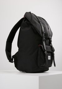 Czarny plecak wykonany z trwałego materiału, z regulowanymi paskami, dwiema kieszeniami bocznymi i zapięciami na klips. Teksturalne detale wzdłuż pasków.