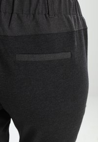 Black sweatpants with a soft fabric texture, featuring an elastic waistband and a back pocket with a horizontal opening.