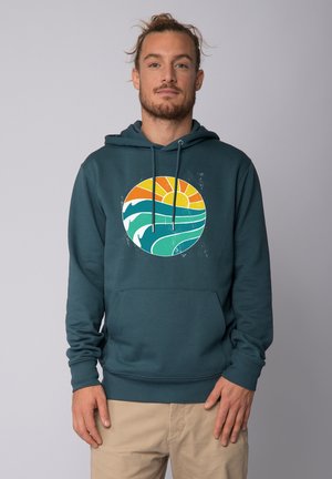 Türkiser Kapuzenpullover mit einem runden Grafikdesign, das Wellen und eine Sonne in orange- und gelbtönen zeigt. Gemütlicher Fleece-Stoff mit einer Vordertasche.