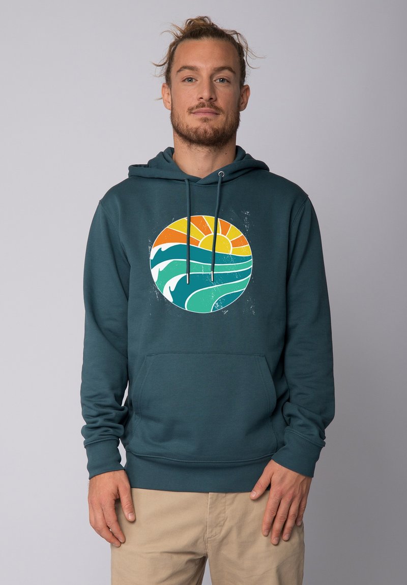 Teal hoodie met een ronde grafiek van golven en een zon in oranje en gele tinten. Comfortabele fleece stof met een frontzak.