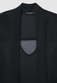 Schwarzer leichter Kimono mit offenem Design, strukturiertem Stoff und einem V-förmigen Ausschnitt in der Mitte. Das Etikett trägt die Aufschrift "CALLIOPE", Größe S.