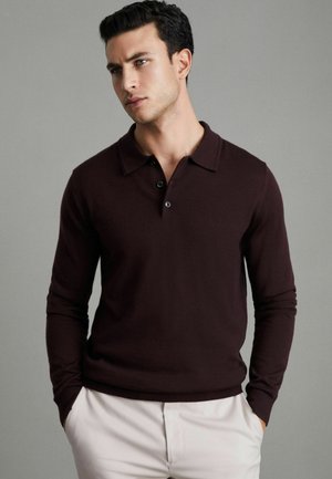 Polo a maniche lunghe color marrone scuro con colletto, caratterizzato da un patta con tre bottoni neri. Realizzato in un morbido tessuto testurizzato.