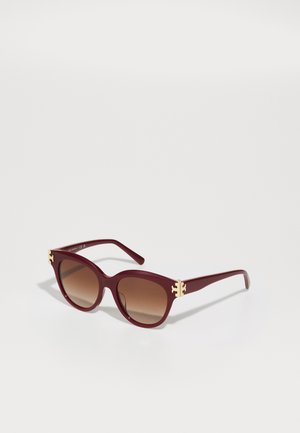 Óculos de sol oversized burgundy com lentes castanhas degradê, apresentando acabamentos em metal dourado nas armações e um acabamento em plástico suave.