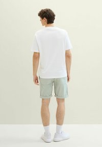 Bia�ła bawełniana koszulka, widok z tyłu, w połączeniu z jasnymi zielonymi, podwiniętymi szortami i białymi trampkami. Gładka tekstura i prosty design.