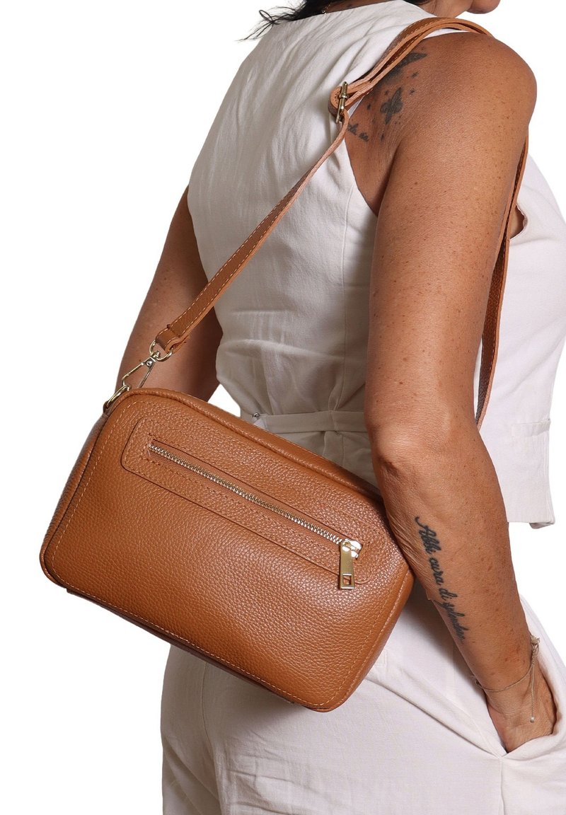 Borsa a tracolla in pelle marrone con texture, tasca frontale con zip, tracolla regolabile e hardware in tonalità oro, mostrata su una persona.