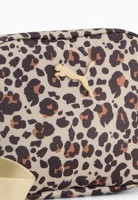 Pussikott leopardimustriga koos tekstuurse kangaga, millel on mustad, pruunid ja beežid täpid, ning beež rihm koos beeži Puma logoga.