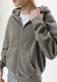 Gray zip-up hoodie made of soft fabric, featuring a front pocket, ribbed cuffs, and a drawstring adjustable hood.