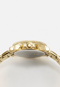 Gold-tone wristwatch with a circular case and textured bezel. Features five pushers and a metal bracelet with a polished finish.