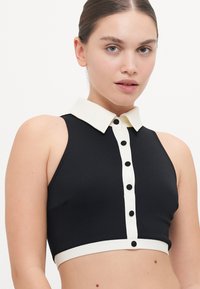 Black cropped top with a white collar and button front. Textured fabric with a fitted design and contrasting white band at the hem.