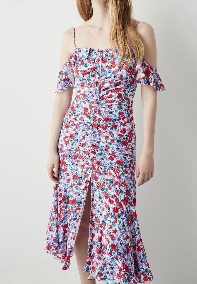 Robe florale avec des motifs rouges et bleus sur fond blanc, dotée de manches dénudées et d'une fente sur le côté dans un design fluide.