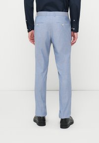 Šviesiai mėlynos pritaikytos kelnės, pagamintos iš tekstūruoto audinio. Yra dvi galinės kišenės su sidabriniais mygtukais ir tiesios kojos dizainas.