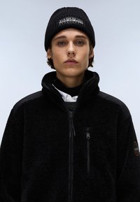 Μαύρο φλις μπουφάν με ψηλό γιακά, φερμουάρ μπροστά και πλαϊνές τσέπες. Περιλαμβάνει ριμπ μαύρο καπέλο με λογότυπο μπροστά.