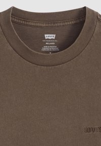 Tricou din bumbac maro, cu o croială relaxată. Prezintă un guler rotund cu margine ribbed și un mic logo brodat Levi's aproape de tiv. Eticheta de îngrijire este vizibilă.