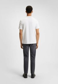 Hvid kortærmet T-shirt parret med mørkegrå jeans og sorte sko. Glat stof med rund hals-design. Enkel, klassisk stil.