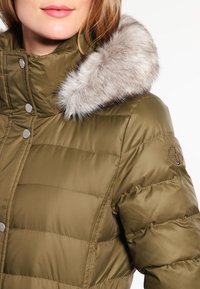 Olivgrön pufferjacka med en avtagbar, ljusgrå fuskpälskrage. Har tryckknappar, quiltad textur och logo på ärmen.