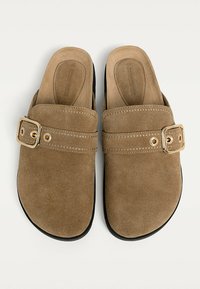 Brown suede slip-on shoes with a gold buckle detail and contrast stitching. Rounded toe and black rubber sole.