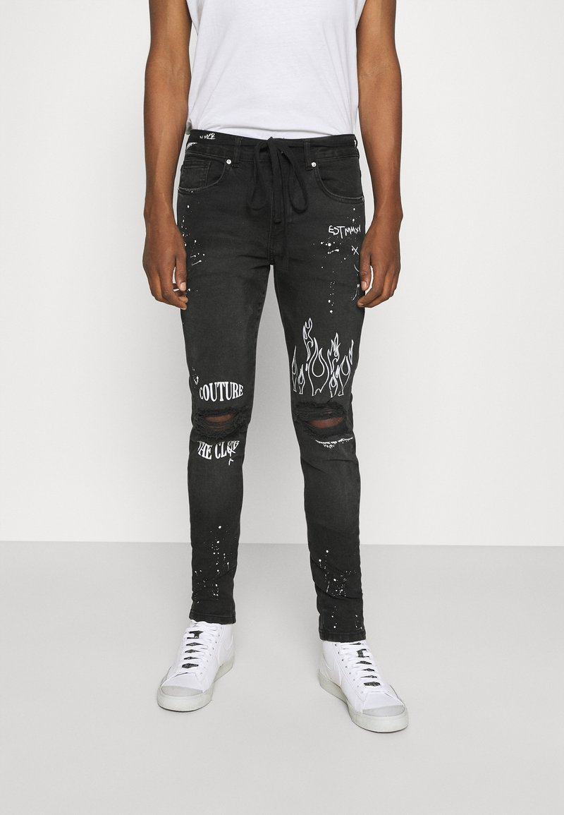 Black denim jeans with distressed detailing, white graphic prints, and a relaxed fit. Features rips at the knees and adjustable waistband.