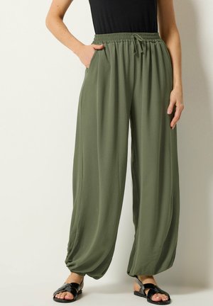 Osoba nosząca luźne oliwkowozielone spodnie z elastycznym pasem i sznurkiem, w połączeniu z czarnymi sandałami i czarnym topem.
