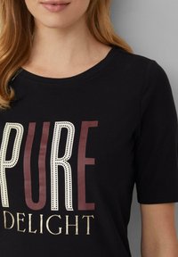 T-shirt noir à manches courtes avec le texte "PURE DELIGHT" en blanc et bordeaux, avec une texture de tissu lisse et un col arrondi.