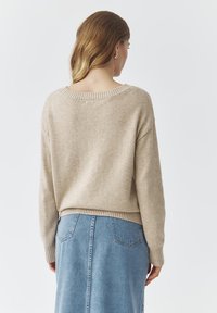 Beige gebreide trui met verlaagde schouders en een ribgebreide zoom, gecombineerd met een lichtblauwe spijkerrok met achterzakken en een rechte snit.