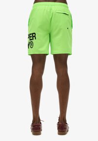 Costumi da bagno verde neon con vita regolabile, dotati di un logo stampato nero sul lato sinistro e di una tasca con zip sul retro.