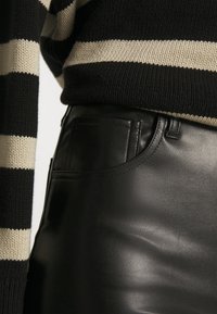 Schwarze Lederhose mit glatter Textur und einer Seitentasche, kombiniert mit einem schwarz-beigen, gestreiften Strickpullover mit lockerem Sitz.