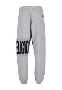 Šedé tepláky vyrobené z jemného materiálu, s velkým černým potiskem "RELIGION" na boku, elastickým pásom a manžetami na nohavicích.