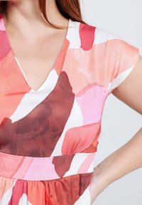 Robe à manches courtes avec un décolleté en V, confectionnée en tissu léger, ornée d'un imprimé abstrait multicolore aux tons rose, rouge et blanc.