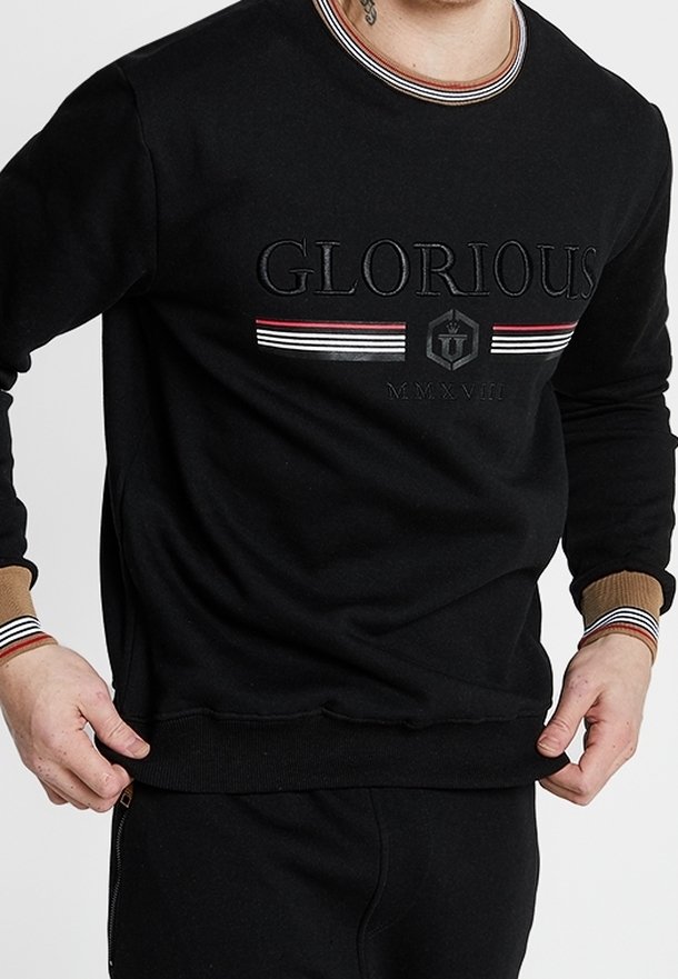 Felpa nera con testo in rilievo "GLORIOUS", dettagli a righe rosse e bianche sul colletto e sui polsini, e bordo a costine. Vestibilità casual.
