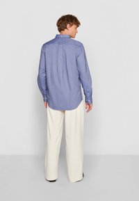 Hellblaues Button-Up-Hemd mit einem Rückenfalten, langen Ärmeln und Knopfmanschetten, kombiniert mit cremefarbenen Hosen. Glatte Stoffstruktur.