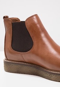 Brown leather ankle boot with a dark elastic side panel, textured sole, and contrasting stitching detail. Smooth finish overall.