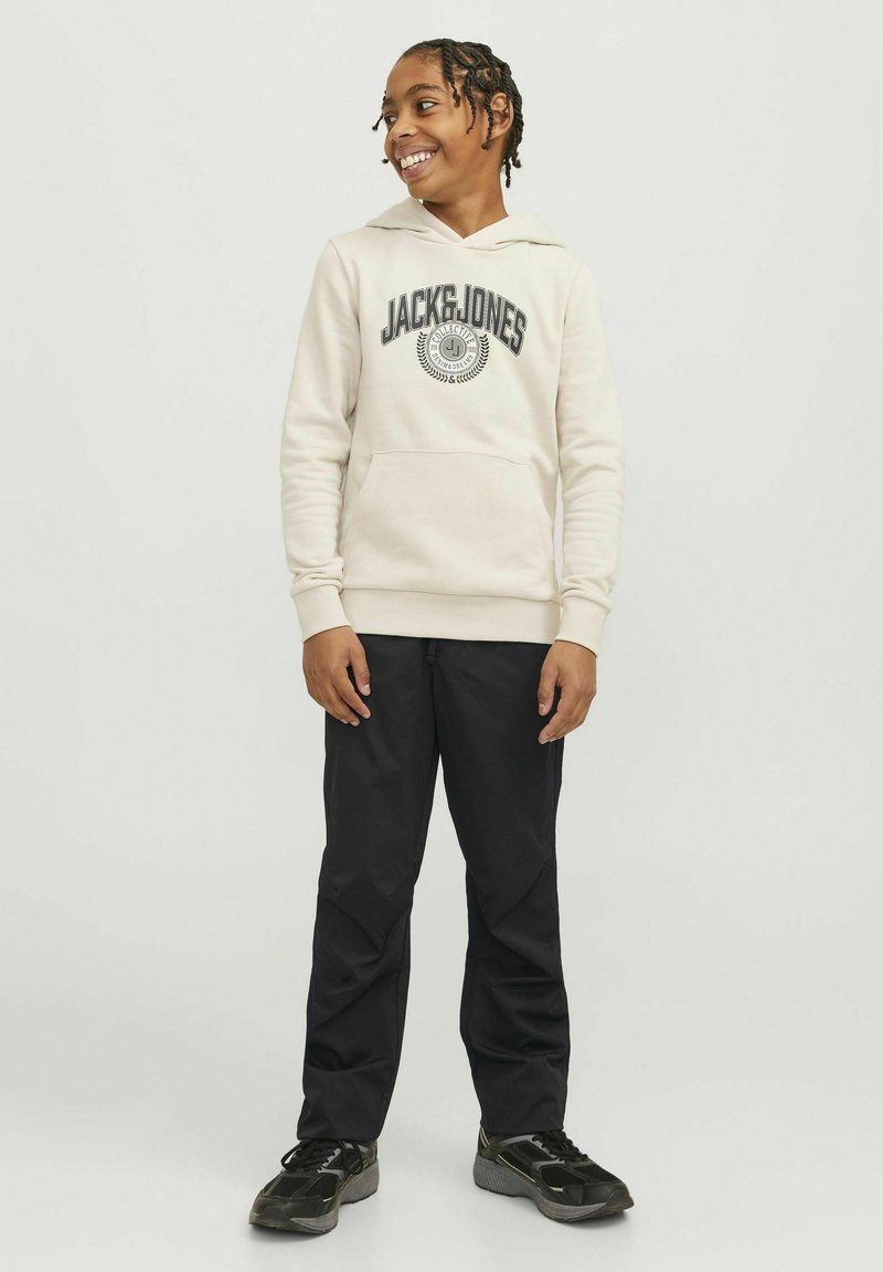 Bež hoodie s logotipom "JACK & JONES", kengurska džep, rebrasti manžeti, uparen s crnim hlačama i crnim tenisicama. Glatka tekstura tkanine.