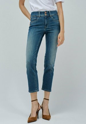 Jeans in denim blu a vita alta, cropped, con macchie sbiadite, chiusura a due bottoni e cinque tasche. Abbinati a tacchi a stiletto marroni.