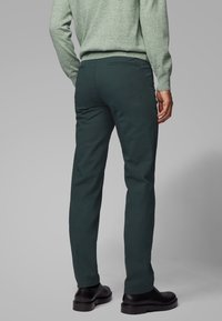 Zielone bawełniane spodnie o dopasowanym kroju, subtelnej fakturze i tylnej kieszeni, zestawione z czarnymi butami i jasnoróżowym swetrem.