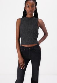 Fekete ujjatlan crop top, amely texturált geometriai mintával rendelkezik, magas derekú fekete farmernadrággal párosítva, amely csillogó díszítésekkel van ellátva.