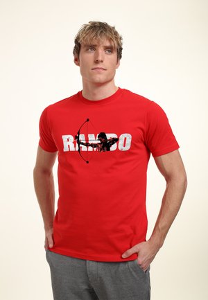 Red cotton t-shirt featuring a graphic of a bow-and-arrow silhouette and the word "RAMBO" in large, distressed white letters.