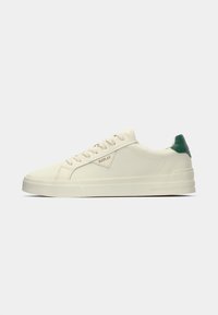 White canvas sneakers with a green heel accent, featuring a lace-up design, textured sole, and a subtle brand logo on the side.