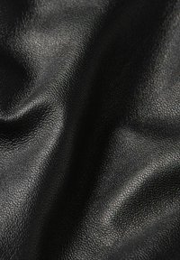 Materiale nero testurizzato con una grana fine e pieghe morbide che creano riflessi e ombre sulla superficie.