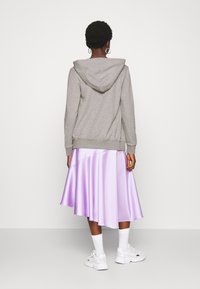 Sweat à capuche gris avec une fermeture éclair latérale et des poignets côtelés, associé à une jupe lavande brillante, complété par des baskets blanches.