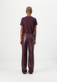 Pantalons en cuir bordeaux à taille haute et poches latérales, associés à un haut sombre ajusté. La texture lisse et la silhouette ajustée sont visibles.