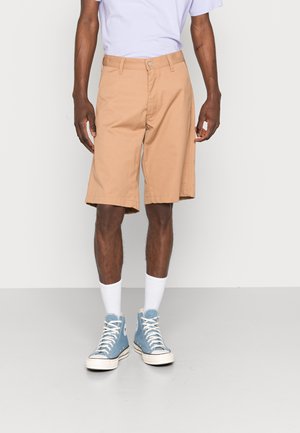 Khaki knælange shorts med lige snit, stofbæltestropper, knaplukning øverst og smalle sidelommer. Kombineret med blå højtopede sneakers.