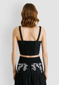 Must have lõhikupla top musta smockeritud seljaga, paksude rihmade ja valge dekoratiivõmblusega. Kandmine musta seeliku koos valgete lilleline tikandega.