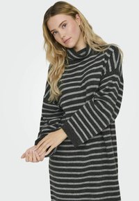 Suéter de punto a rayas en negro y gris, con cuello alto, mangas largas y un corte relajado. Textura suave con patrón de punto visible.