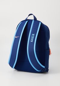 Sinine seljakott pehmendusega disainiga, reguleeritavad õlarihmad, Nike logo ja oranž tõmblukk. Omab kahte tooni värve ja ülemist käepidet.