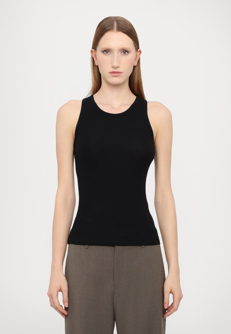 Top nero senza maniche realizzato in un tessuto liscio e elasticizzato. Presenta un collo rotondo e un design aderente, abbinato a pantaloni grigi sartoriali.