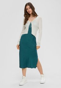 Turkusowa midi sukienka z bocznym rozcięciem i lekkim kremowym kardiganem z zapięciem na wiązanie i długimi rękawami. Połączona z białymi trampkami za kostkę.